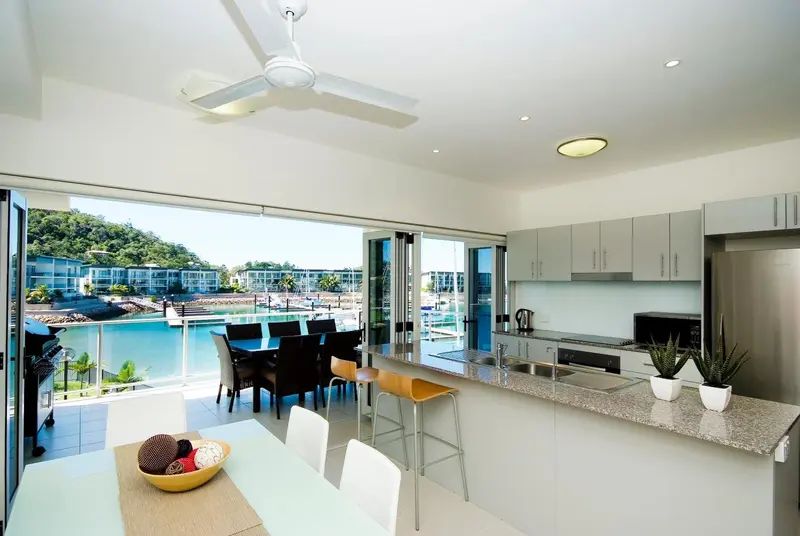 Une cuisine ouverte sur une salle à manger lumineuse avec vue sur un port de plaisance.