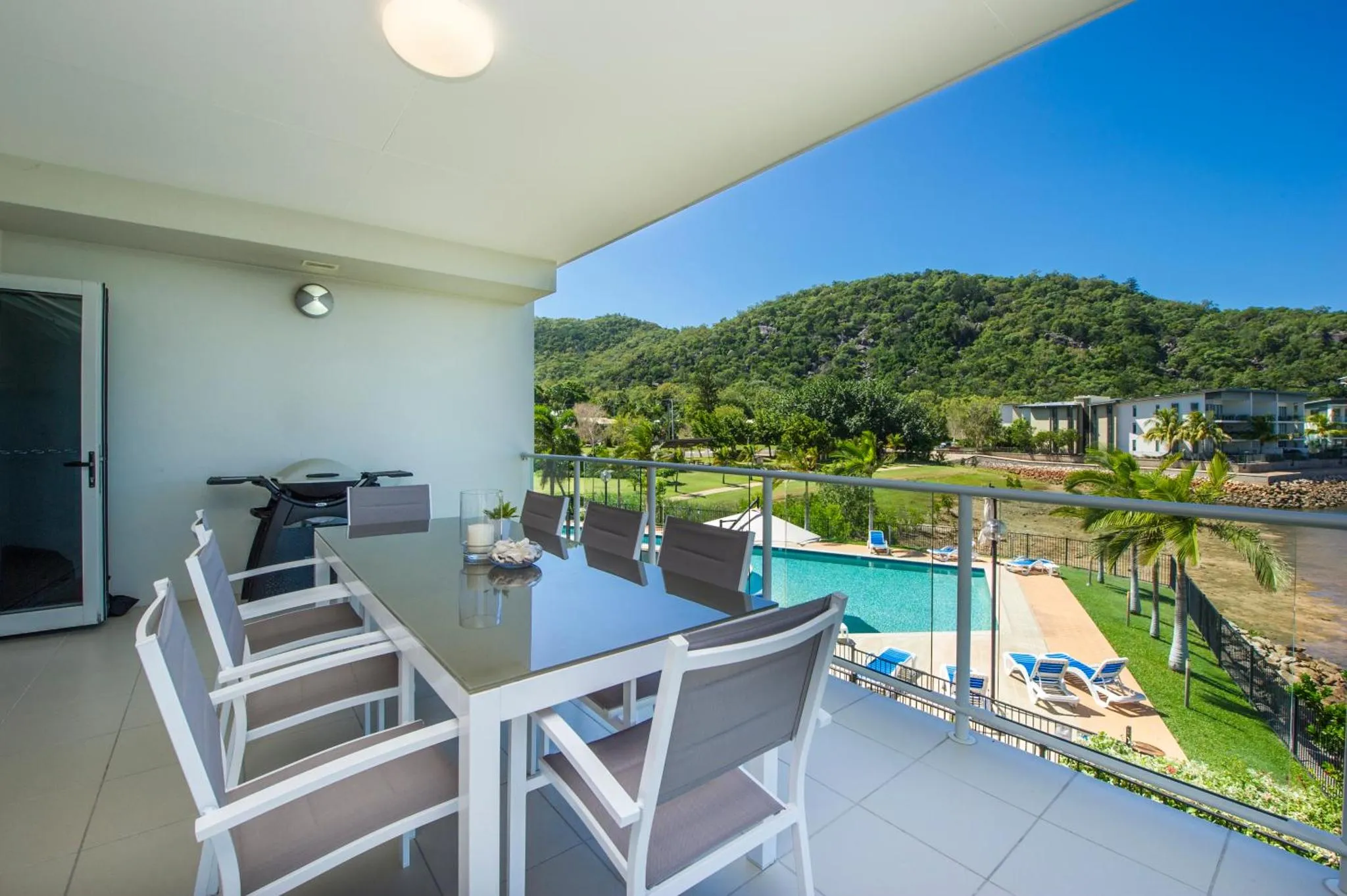 Une table à manger est mise en scène sur une terrasse avec vue sur une piscine et une végétation luxuriante.