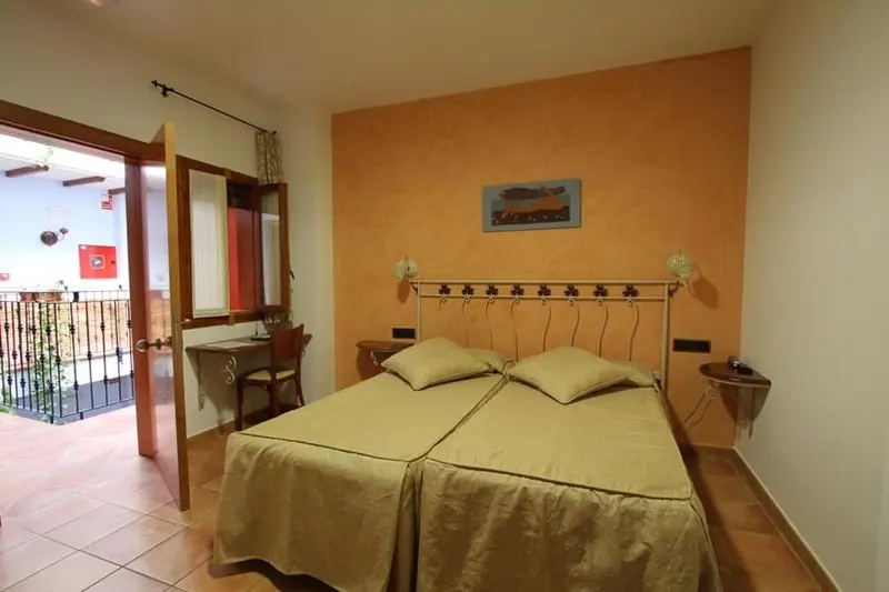 Une chambre lumineuse avec un lit double et un bureau près d'une porte-fenêtre.