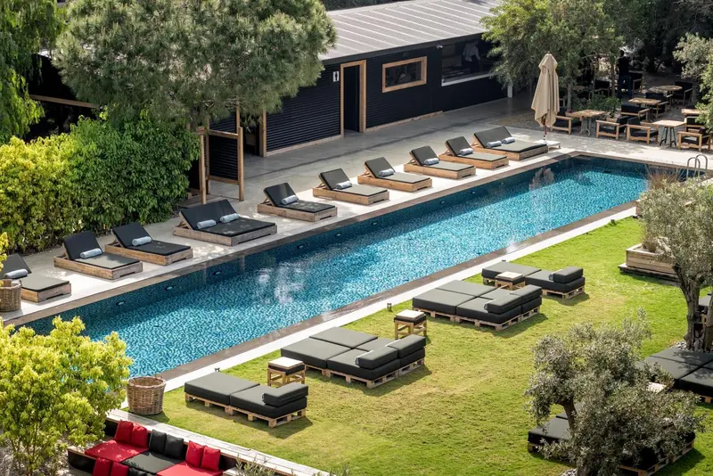 Vue aérienne d'une piscine rectangulaire entourée de transats et d'un jardin verdoyant.