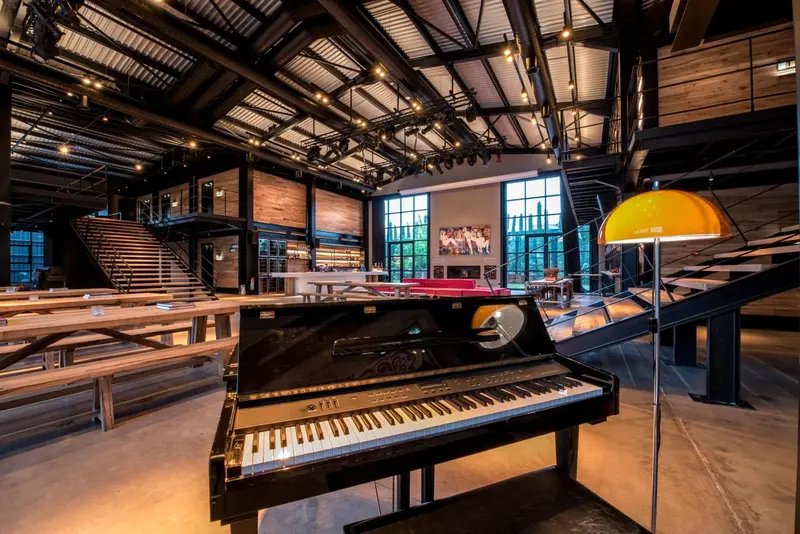 Un piano à queue noir se trouve dans un espace intérieur lumineux avec une mezzanine et de grandes fenêtres.