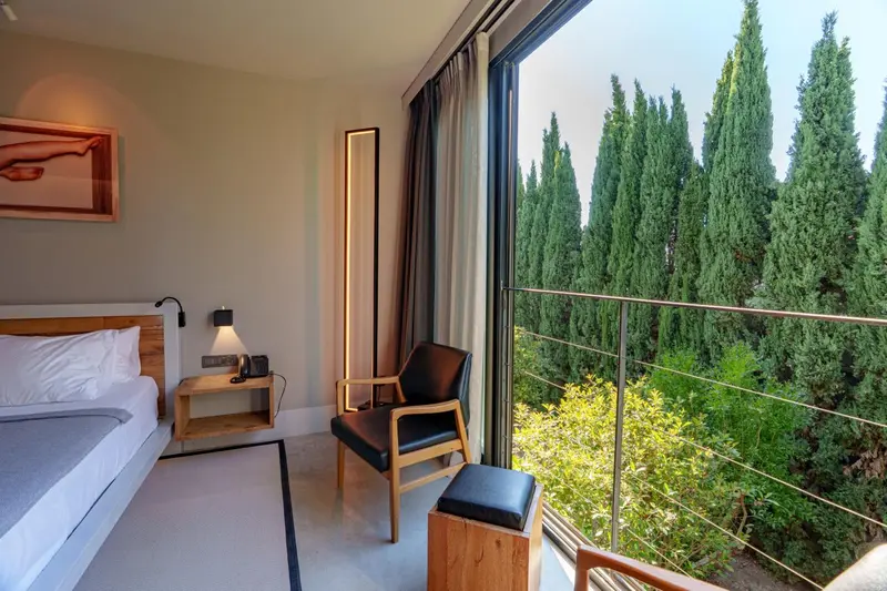 Une chambre lumineuse avec un lit et un fauteuil donnant sur une végétation luxuriante.
