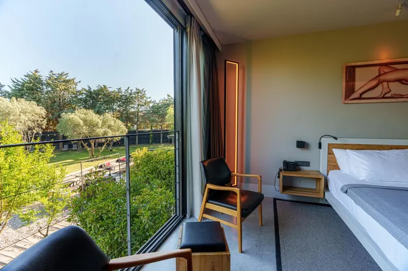 Une chambre lumineuse avec un lit et un fauteuil, donnant sur une terrasse et un jardin verdoyant.