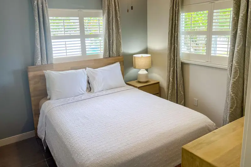 Une chambre lumineuse avec un lit double et des rideaux clairs.