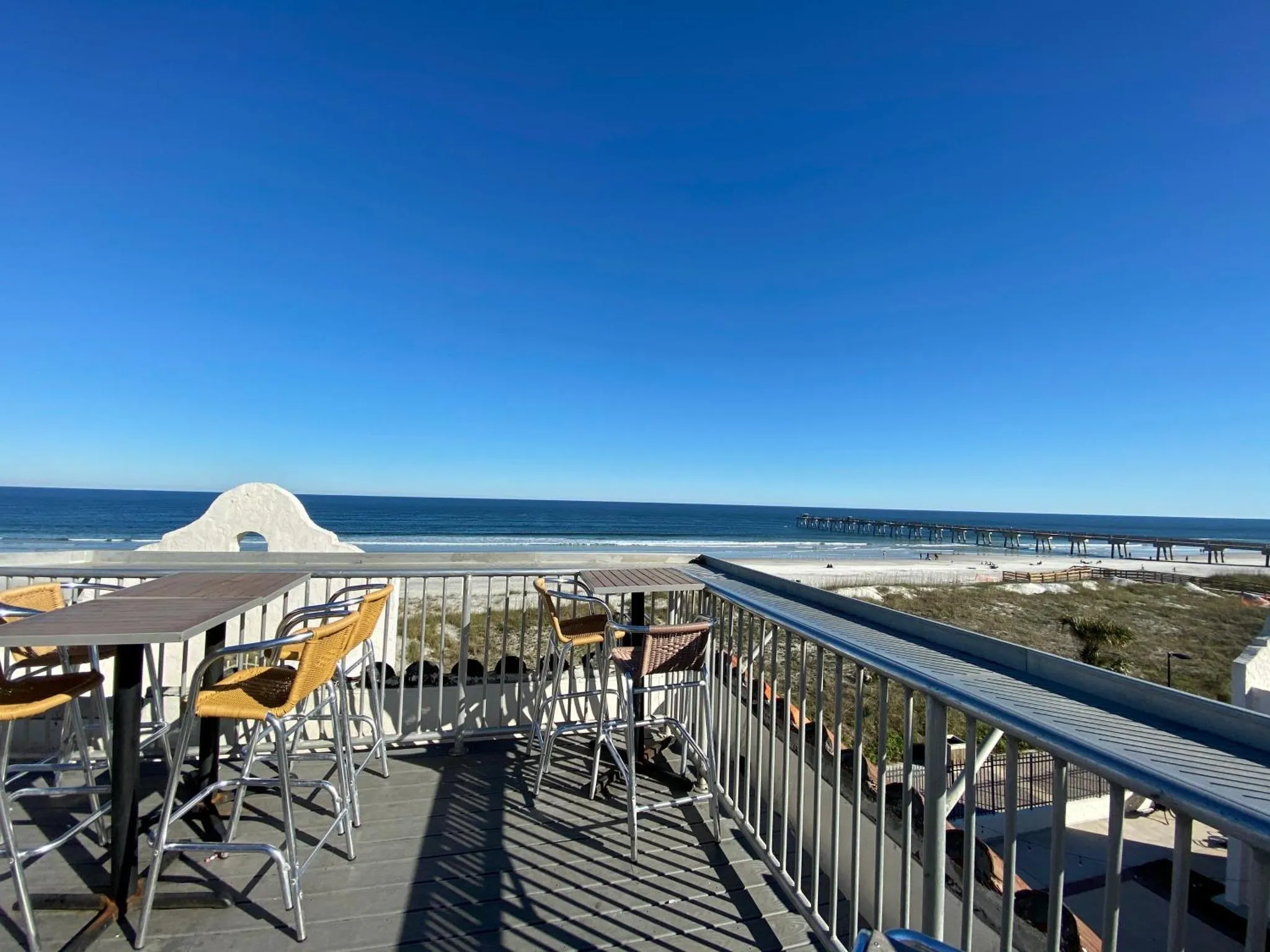 Terrasse avec tables et chaises donnant sur la mer et la plage.