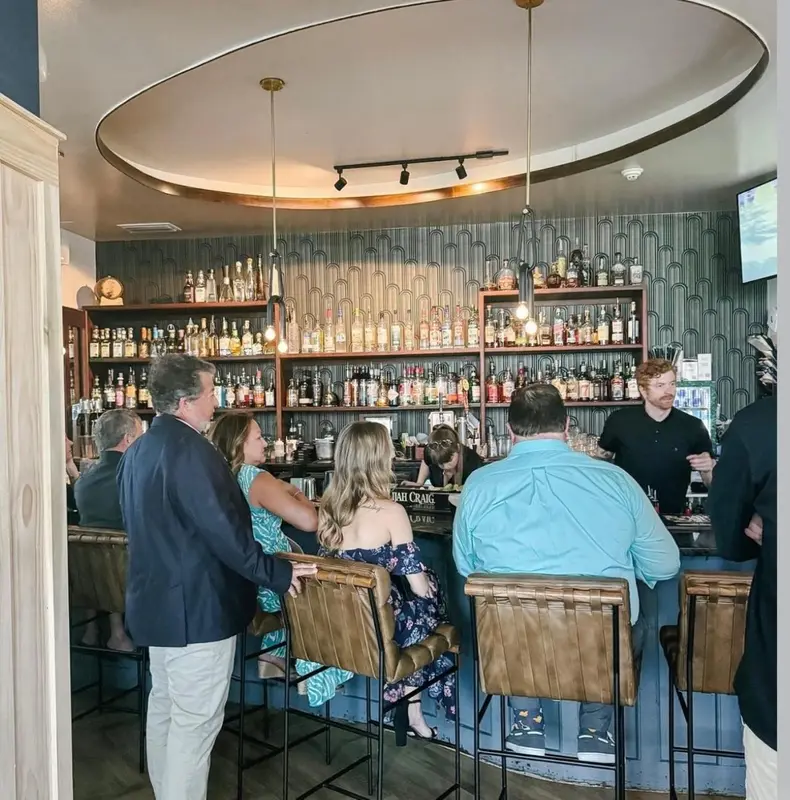 Un comptoir de bar est fréquenté par des clients assis sur des tabourets.