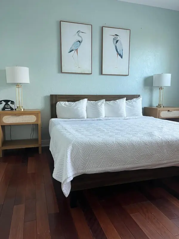 Une chambre lumineuse avec un grand lit recouvert d'une courtepointe blanche et deux tableaux représentant des oiseaux.