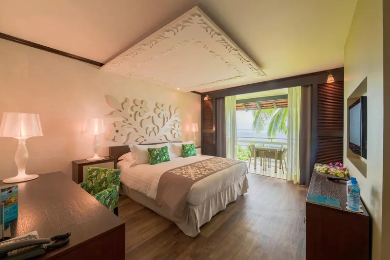 Une chambre lumineuse avec un lit double donnant sur une terrasse et la mer.