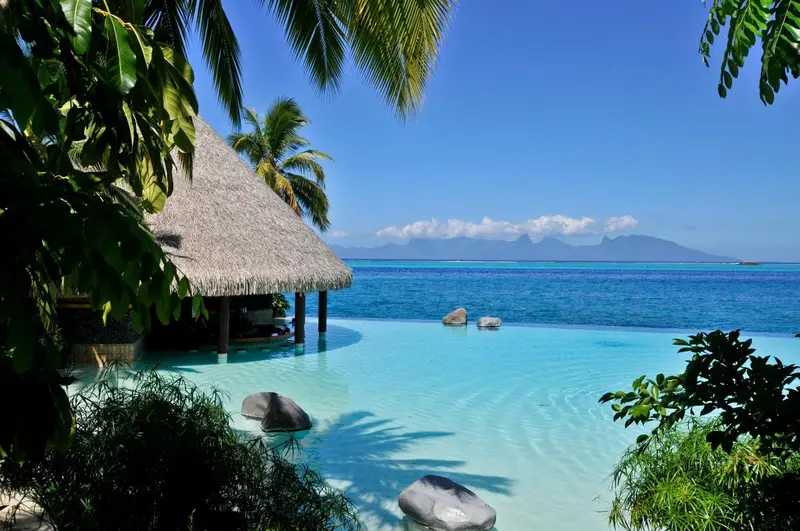 Une piscine turquoise bordée de rochers et de végétation tropicale offre une vue sur la mer.