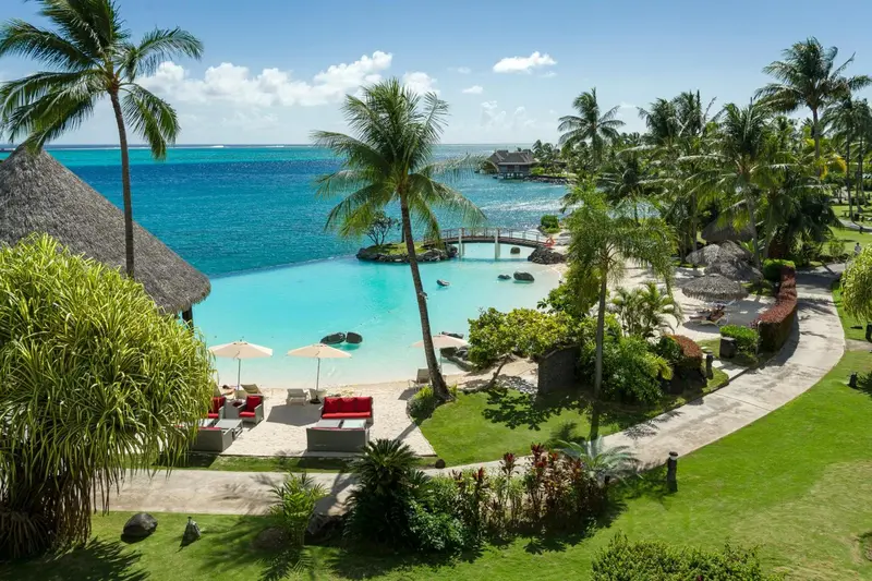 Vue aérienne d'une piscine turquoise bordée de chaises longues et de végétation tropicale.