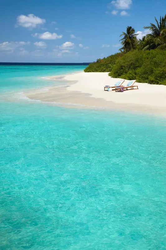 Deux transats bleus sur une plage de sable blanc bordée d'eau turquoise.