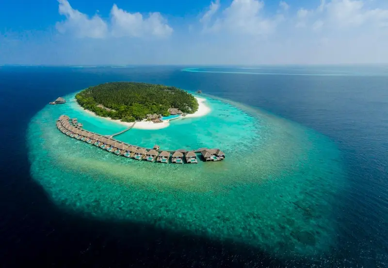 Vue aérienne d'une île tropicale avec des bungalows sur pilotis et une plage de sable blanc.