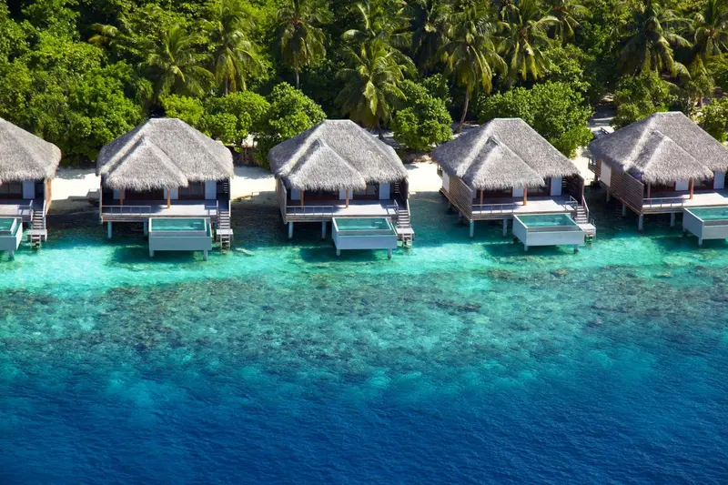 Vue aérienne de bungalows sur pilotis au-dessus d'un lagon turquoise.