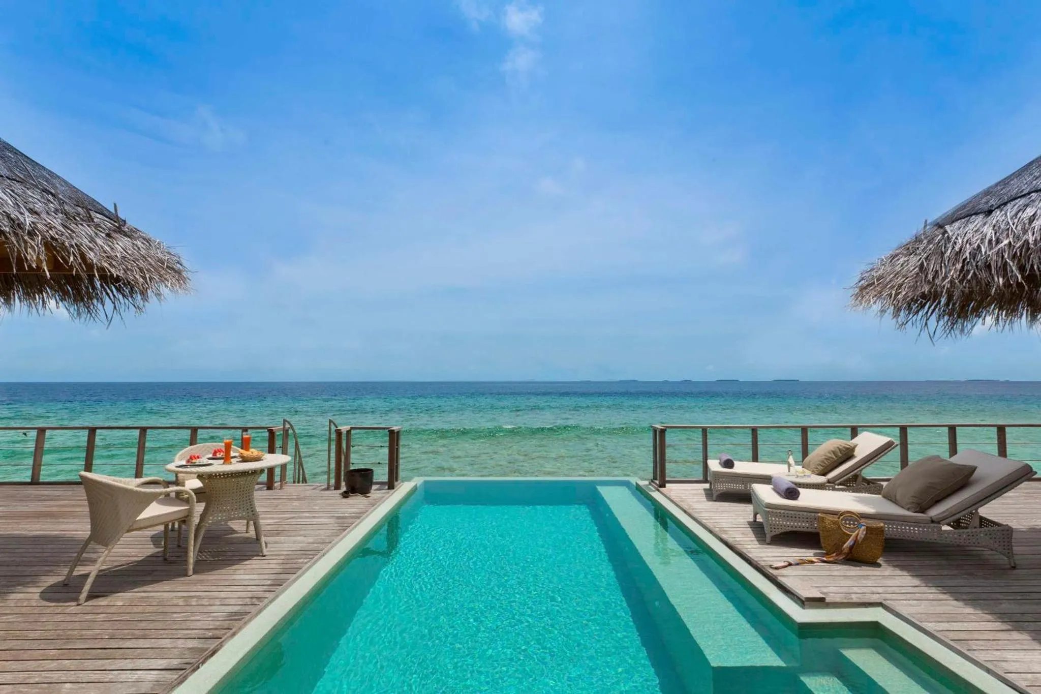Terrasse en bois avec piscine et transats face à la mer.