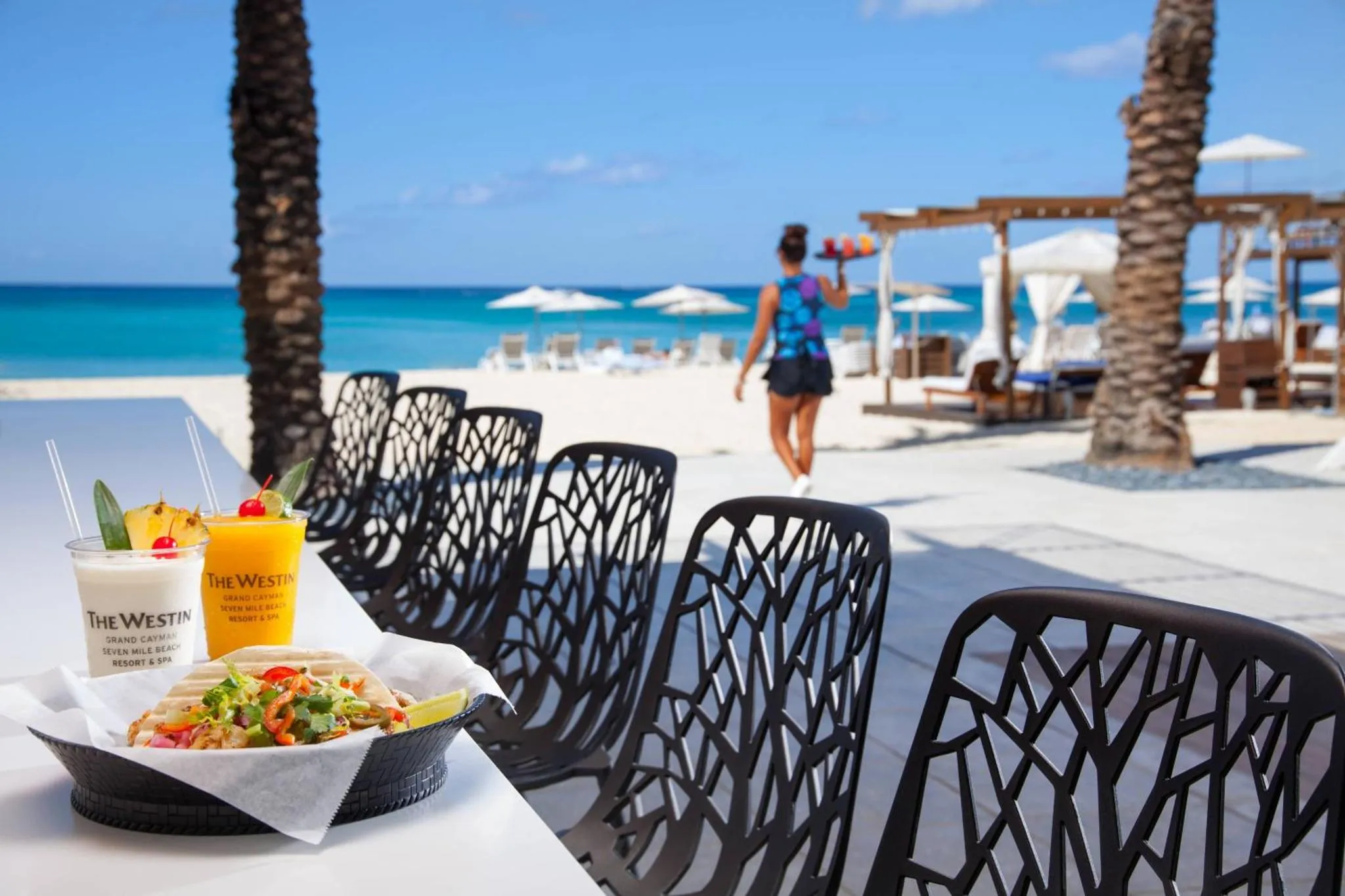 Une table de restaurant avec des plats et des boissons en terrasse face à la mer.
