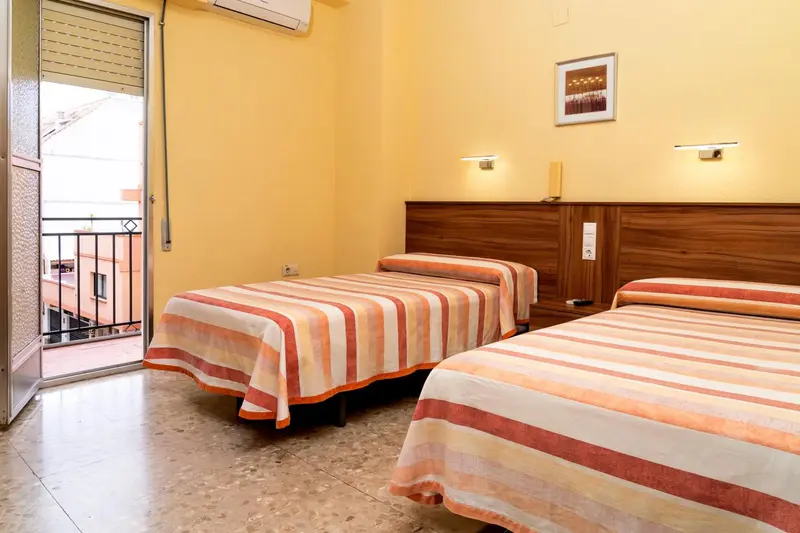 Chambre lumineuse avec deux lits simples et balcon.
