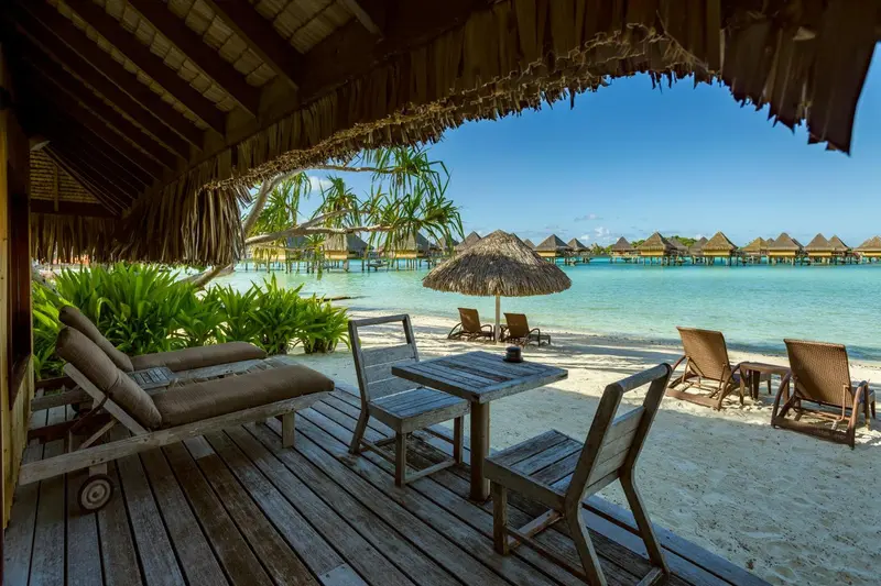 Terrasse en bois avec mobilier de jardin donnant sur une plage de sable blanc et une mer turquoise.