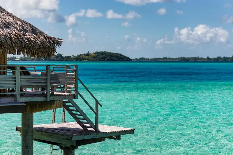 Terrasse en bois donnant sur une eau turquoise et une île verdoyante.