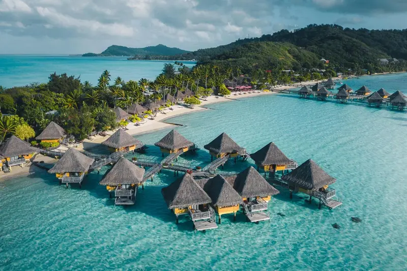 Vue aérienne d'un ensemble de bungalows sur pilotis au-dessus d'une lagune turquoise.