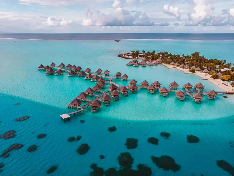 Vue aérienne d'un ensemble de bungalows sur pilotis au-dessus d'un lagon turquoise.