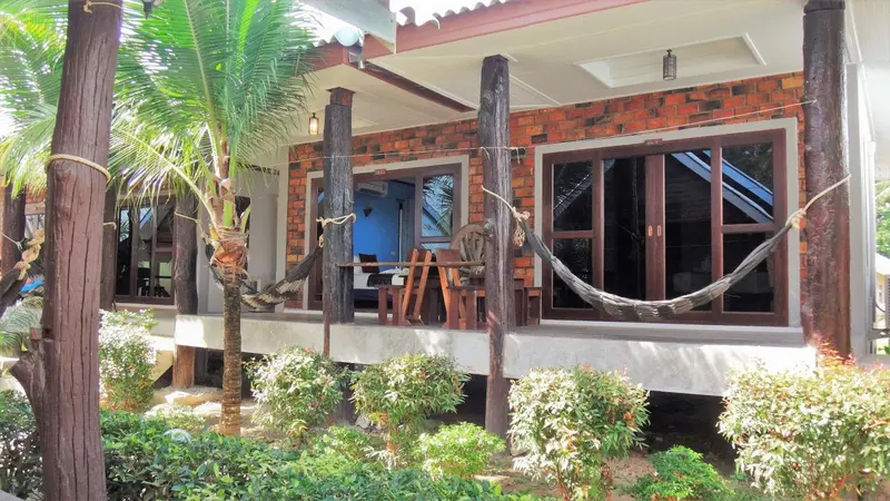 Terrasse ombragée avec hamac devant un bâtiment en briques.