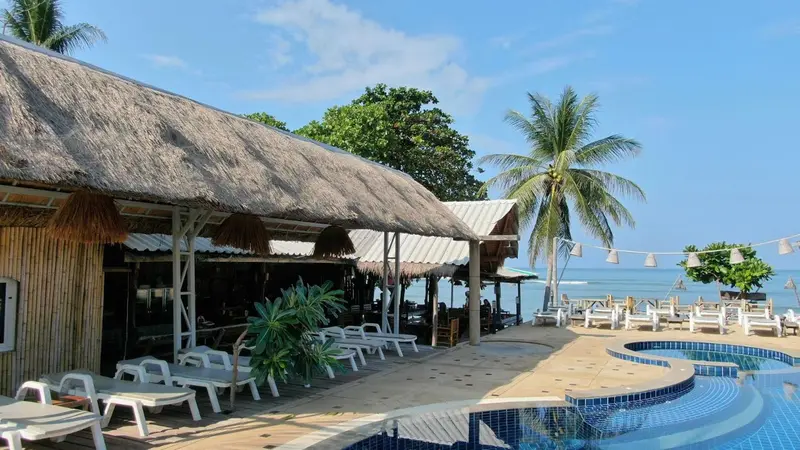 Terrasse ombragée avec chaises longues donnant sur une piscine et la mer.