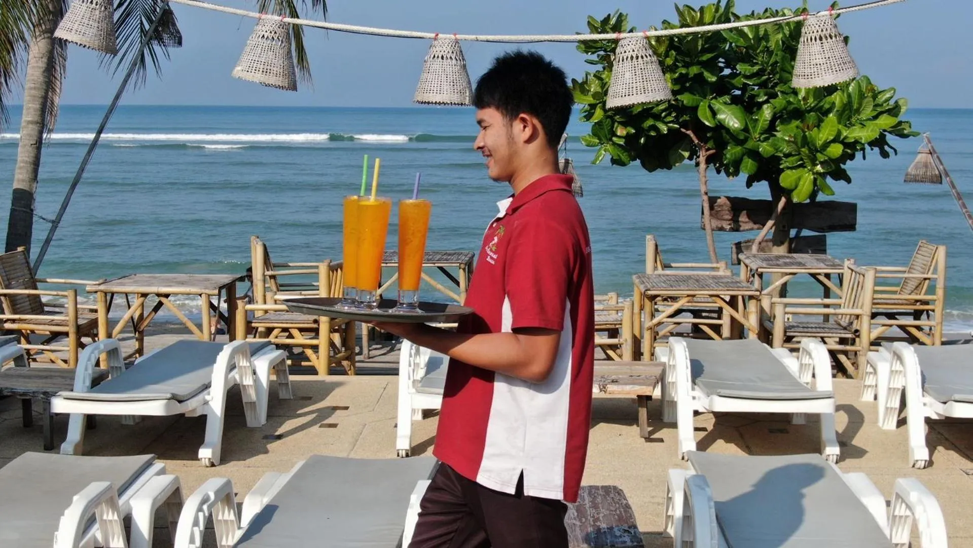 Un serveur porte des boissons fraîches sur un plateau au bord de la mer.