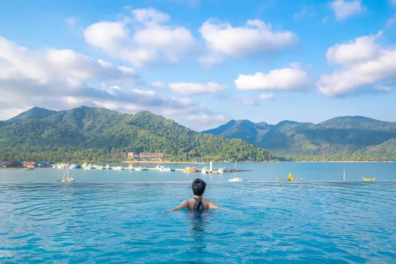 Une personne se détend dans une piscine à débordement face à la mer et aux montagnes.