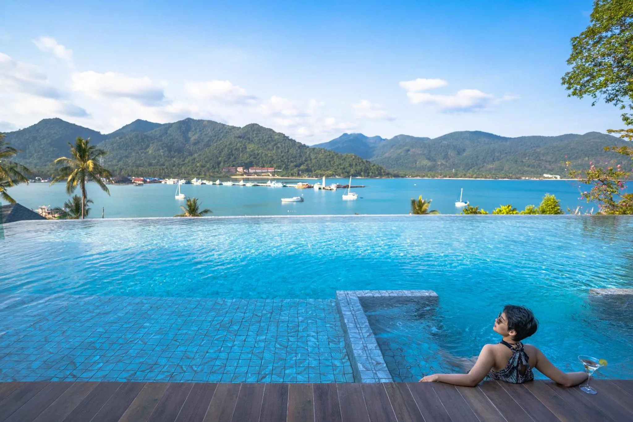 Une personne se détend au bord d'une piscine à débordement avec vue sur la mer et les montagnes.