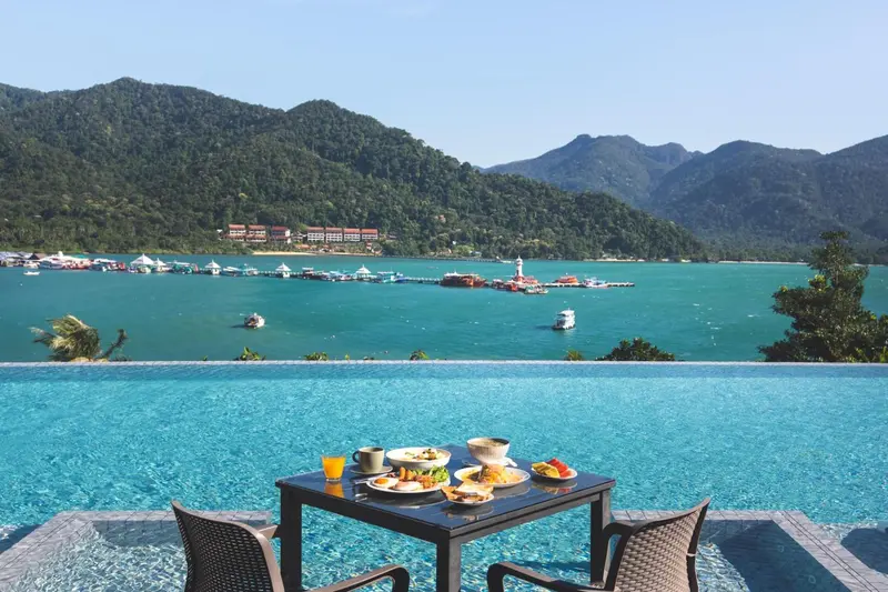 Une table de petit-déjeuner est dressée au bord d'une piscine à débordement avec vue sur une baie.