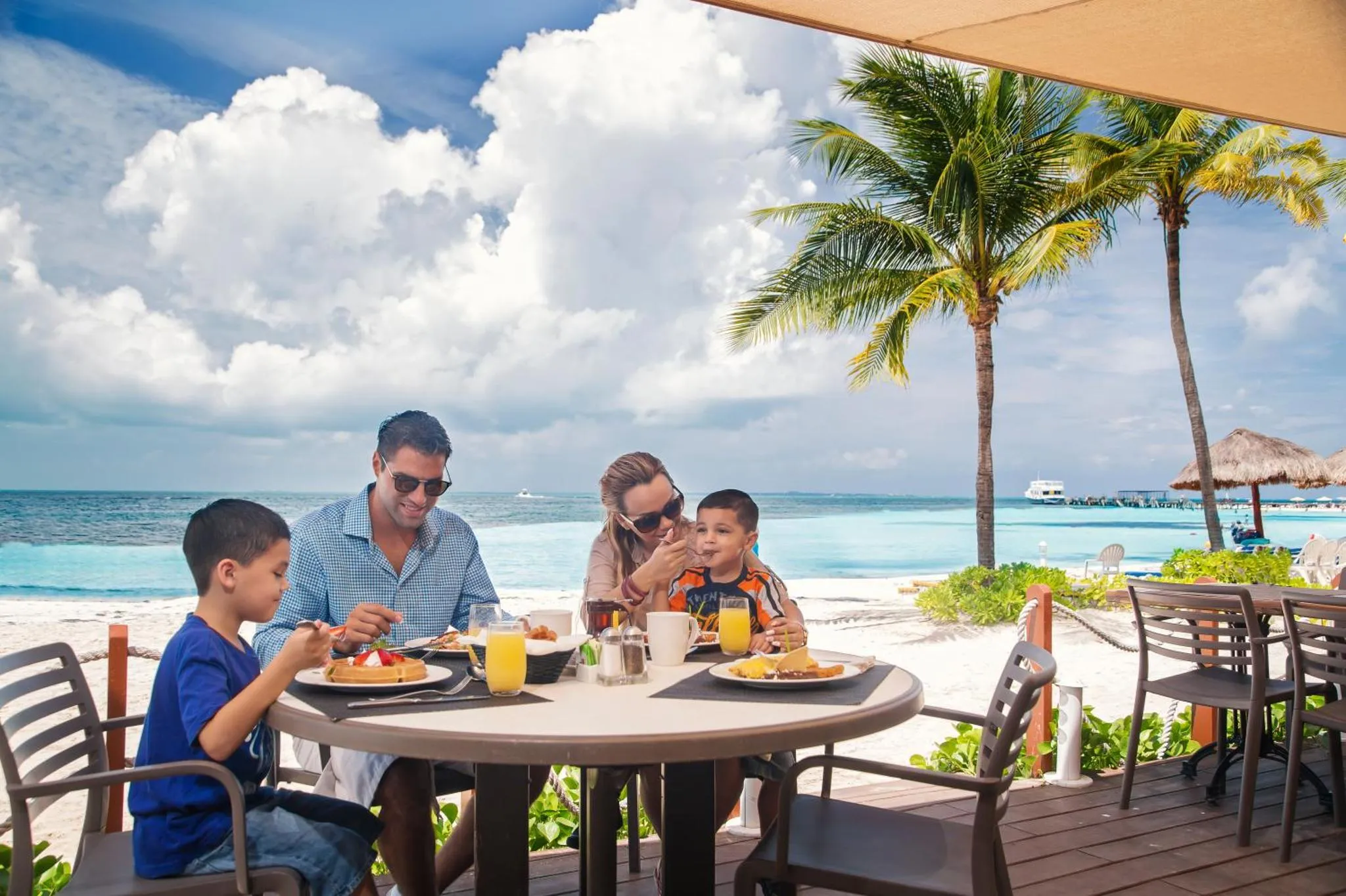 Une famille prend son petit-déjeuner à une table en extérieur face à la mer.