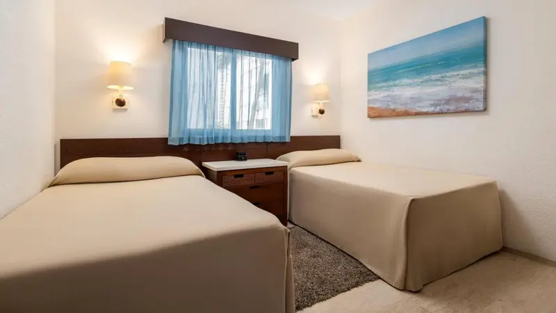 Une chambre lumineuse avec deux lits simples et un tableau représentant la mer.