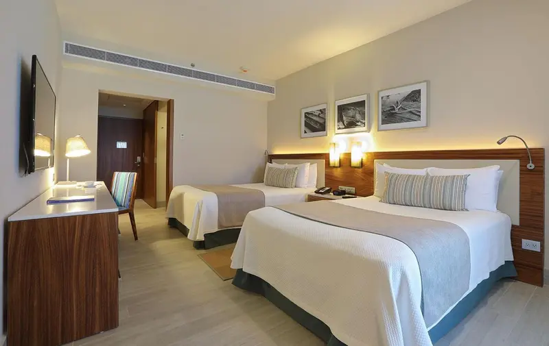 Une chambre d'hôtel lumineuse avec deux lits simples et un bureau.