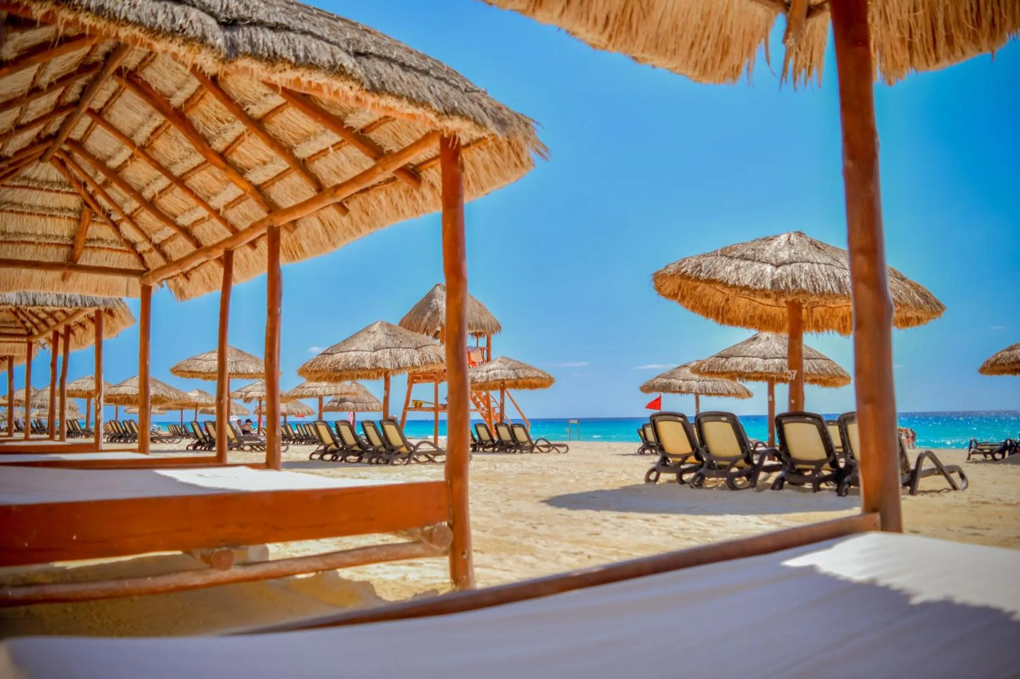 Transats et parasols de plage sous des toits de chaume, vue sur la mer.
