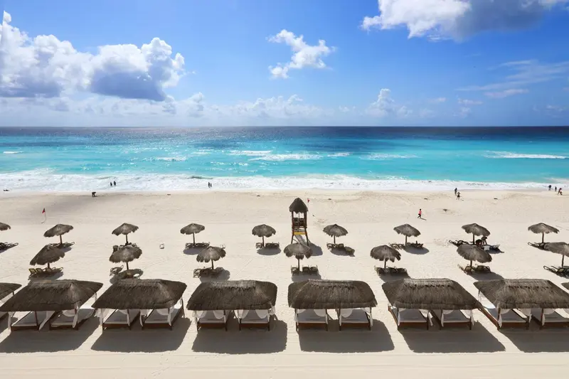 Plage de sable blanc bordée d'une mer turquoise et de parasols.