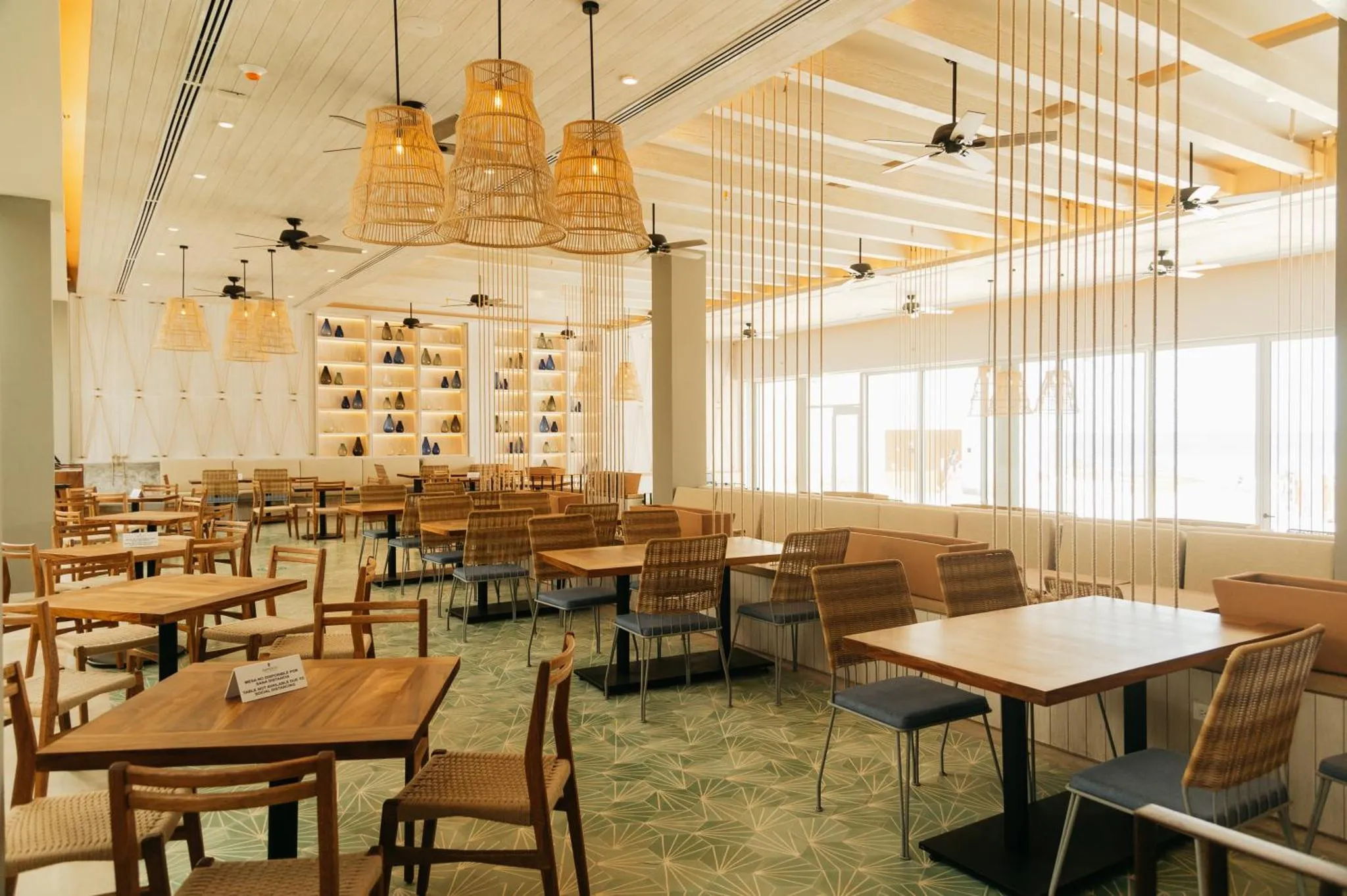 Une salle lumineuse avec de nombreuses tables et des luminaires suspendus en osier.