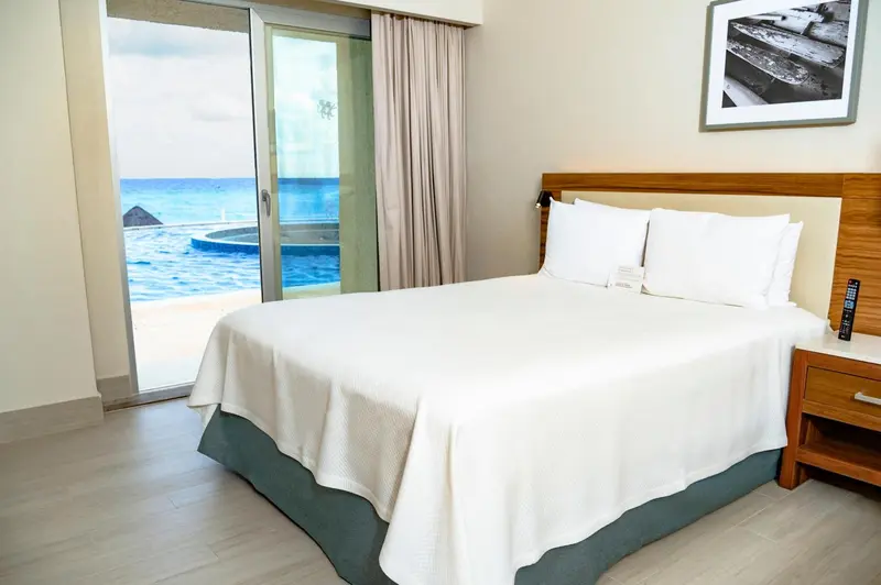 Une chambre lumineuse avec un grand lit donnant sur une piscine et la mer.