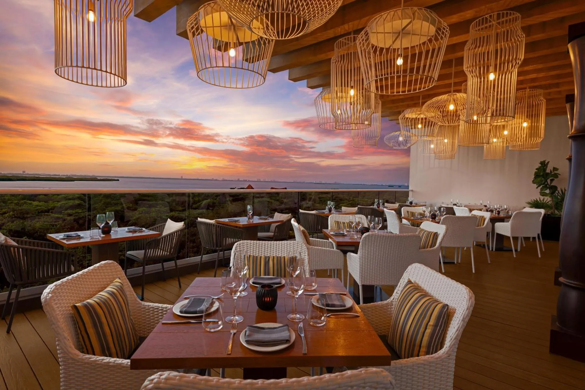 Une terrasse de restaurant avec des tables dressées face à la mer au coucher du soleil.