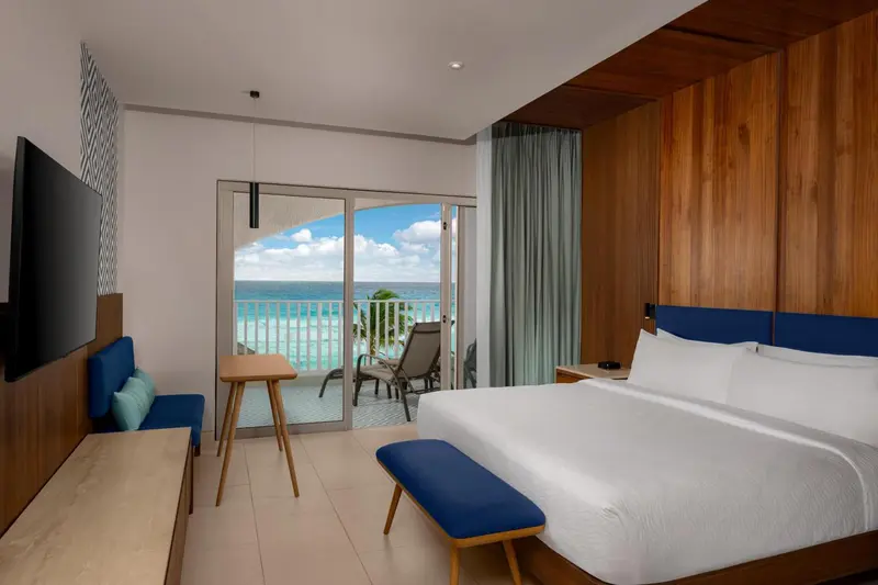 Chambre lumineuse avec un grand lit et une vue sur la mer depuis un balcon.