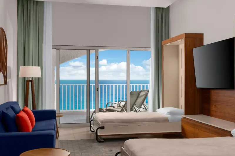 Une chambre lumineuse avec un canapé bleu et une vue sur la mer depuis un balcon.
