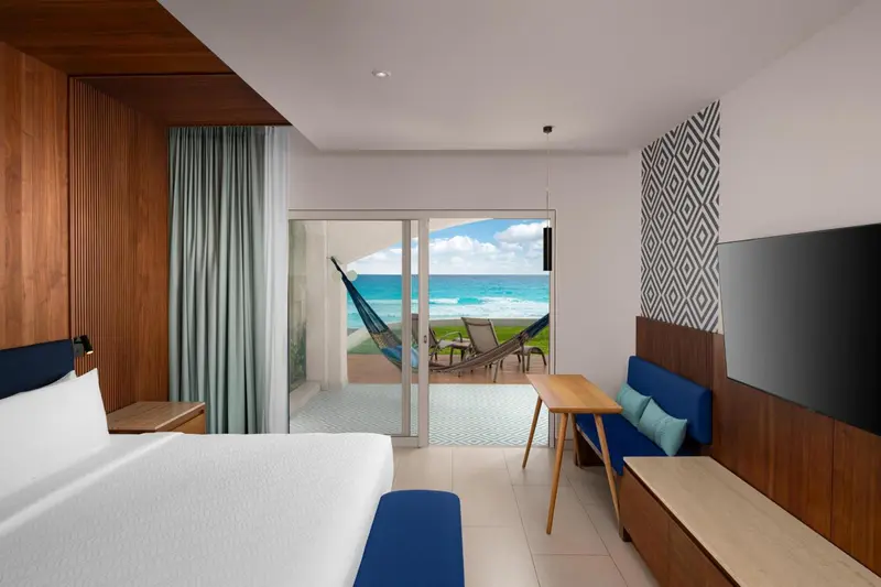 Chambre lumineuse avec un lit blanc et une vue sur la mer depuis une terrasse.