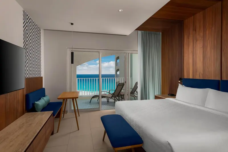 Chambre lumineuse avec un lit blanc et une vue sur la mer depuis un balcon.