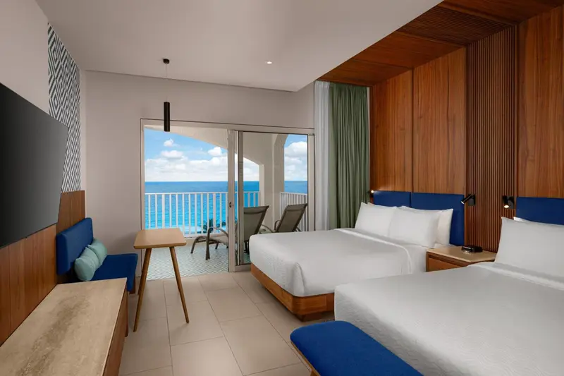 Chambre lumineuse avec un lit double et un accès à un balcon offrant une vue sur la mer.