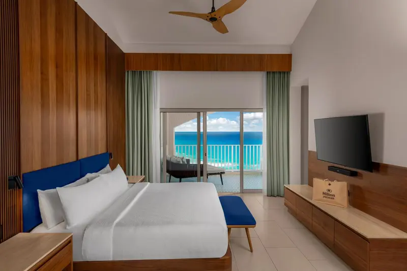 Une chambre lumineuse avec un grand lit face à une baie vitrée donnant sur la mer.