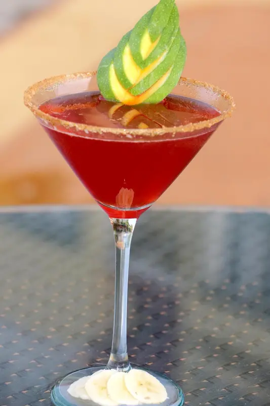 Un cocktail rouge vif est servi dans un verre à martini décoré d'une tranche d'ananas et de sel.