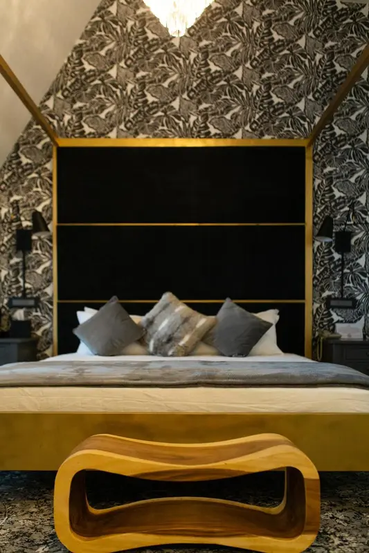 Un lit avec une tête de lit noire et des oreillers gris dans une chambre décorée de papier peint à motifs.