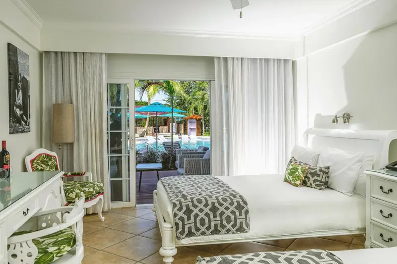 Chambre lumineuse avec un lit recouvert d'une couverture à motifs et vue sur une piscine.