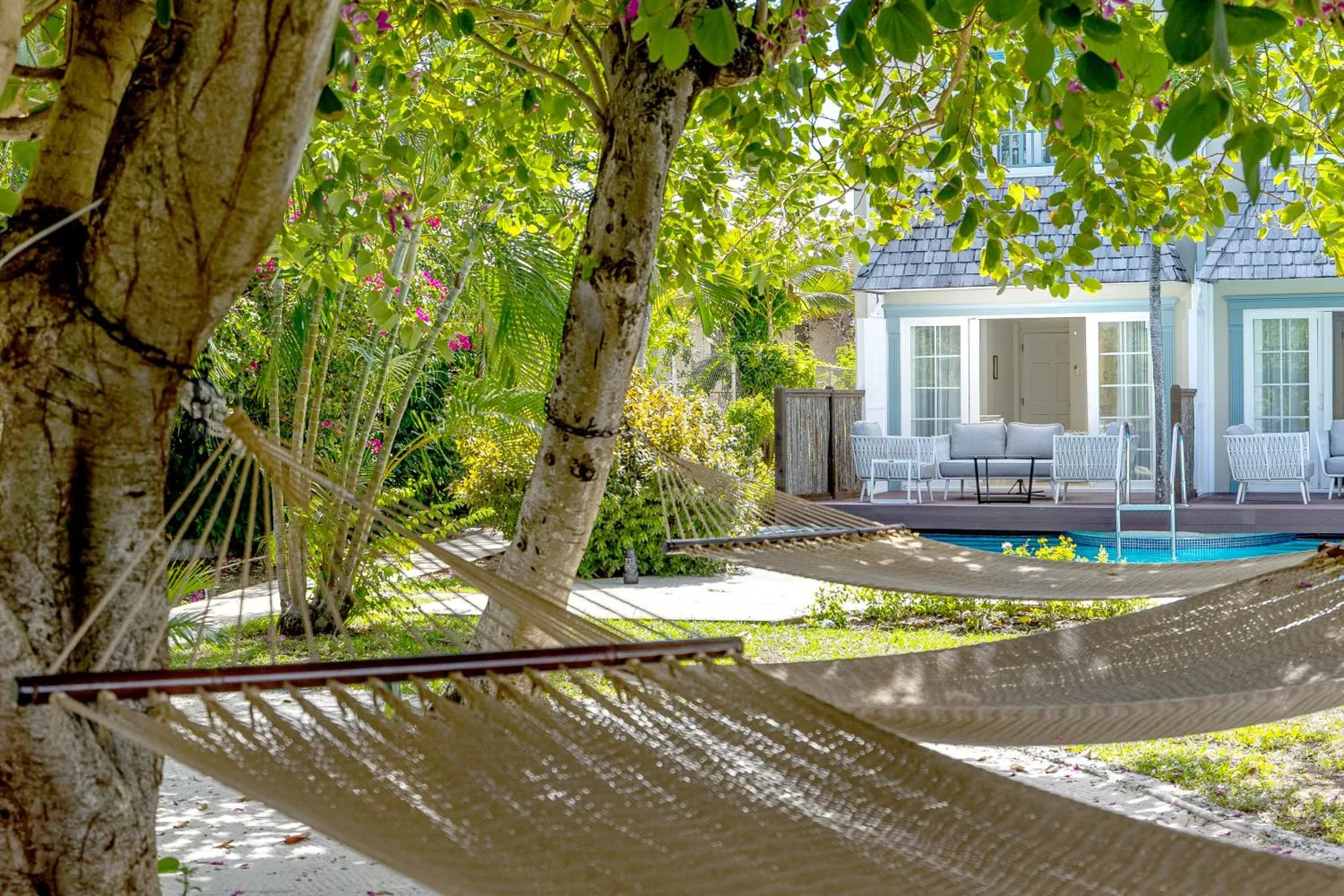 Deux hamacs sont tendus entre les arbres, face à une piscine et à un bâtiment clair.
