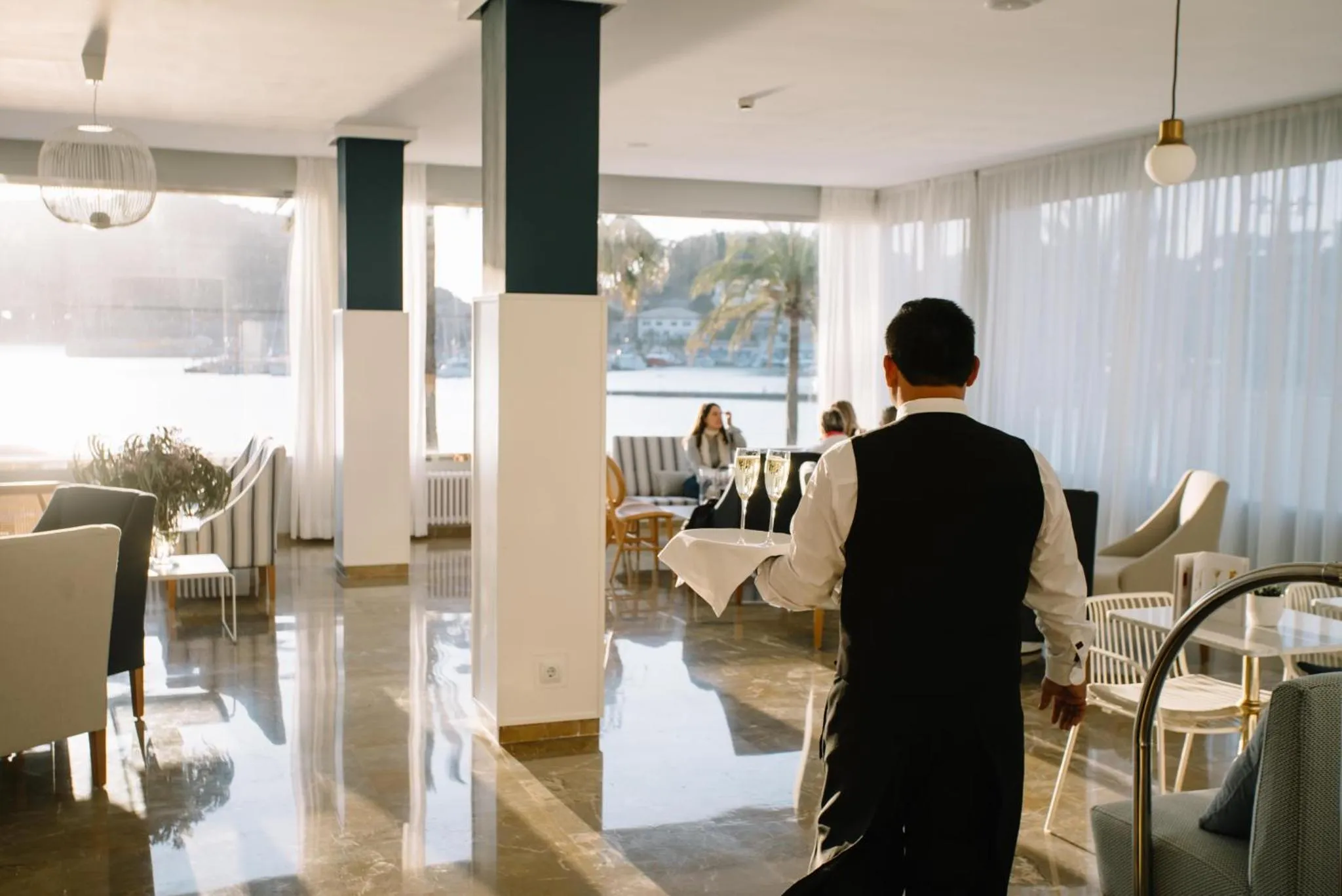 Un serveur porte des verres dans un espace lumineux avec vue sur la mer.