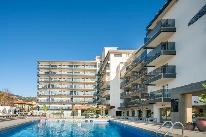 Bâtiment moderne avec des balcons donnant sur une piscine ensoleillée.